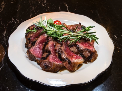 Medium rare steak sliced on a plate and topped with a branch of rosemary