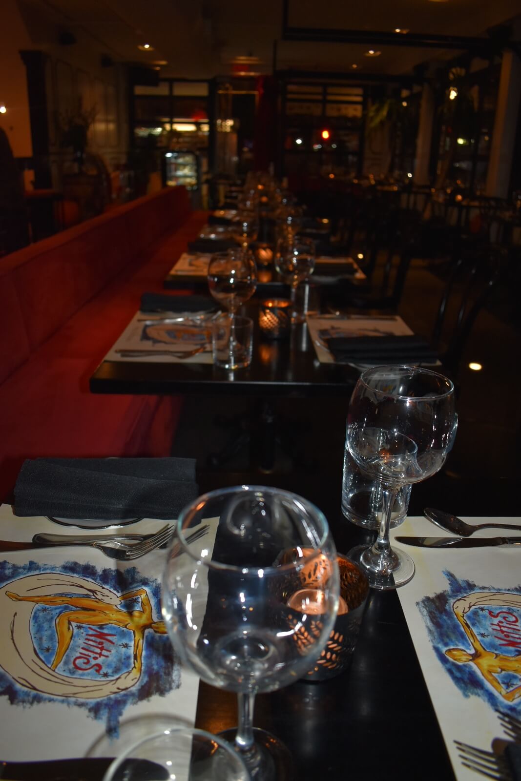 Row of tables against a booth with chairs on the other side. Table settings for two at each