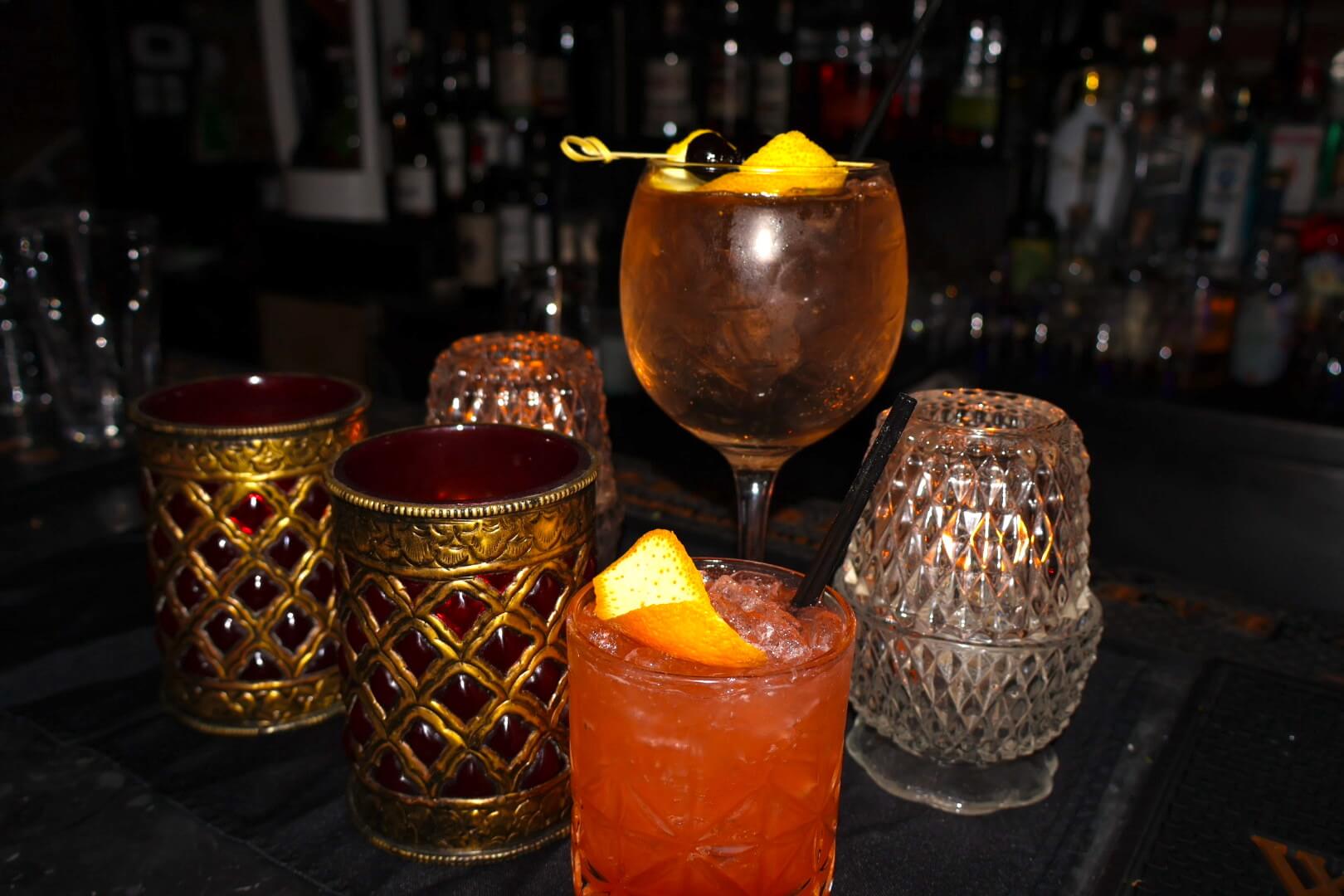 Two cocktails and various pieces of glassware on black bartop