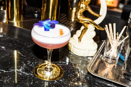 A pink cocktail drink with a blue flower in it