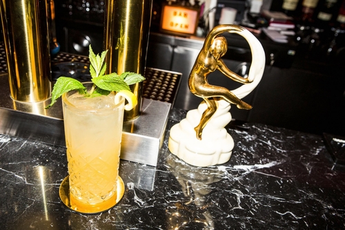 yellow and clear mixed drink with golden Nittis satue next to it on the bar