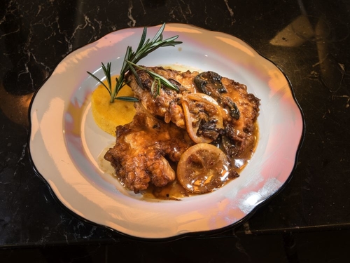 Breaded chicken in a brown sauce with lemon slices and rosemary