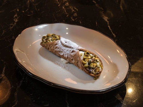 A Cannoli with crushed nuts and powdered sugar on top