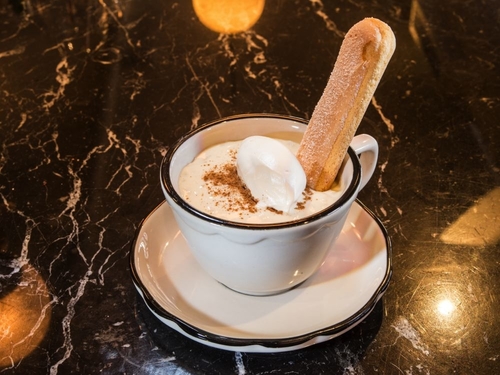 A dessert offee in a white tea cup on a plate with a cinnamon pastry sticking out of it