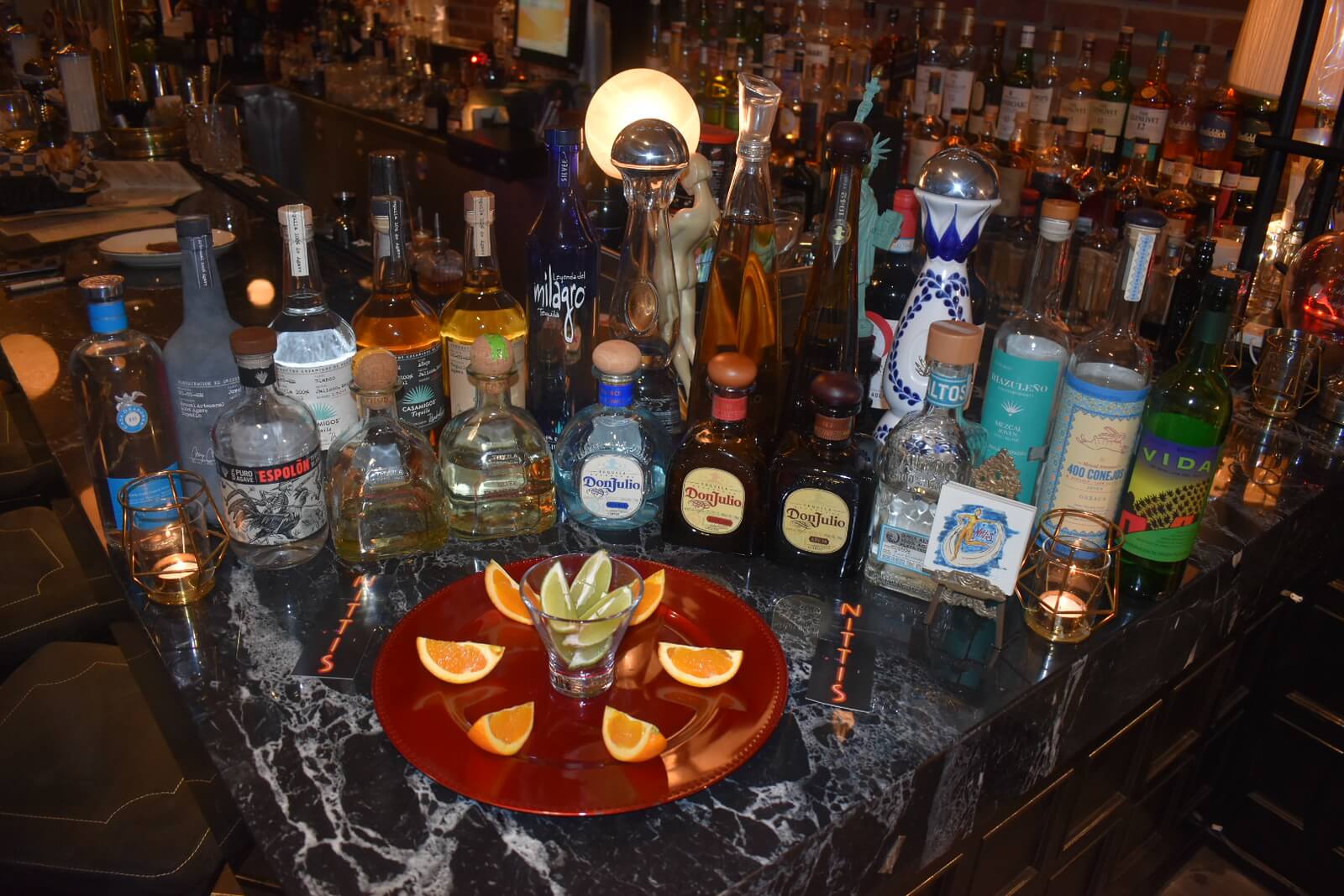 Red plate with a shot glass and citrus slices in front of liquor bottles on the bar